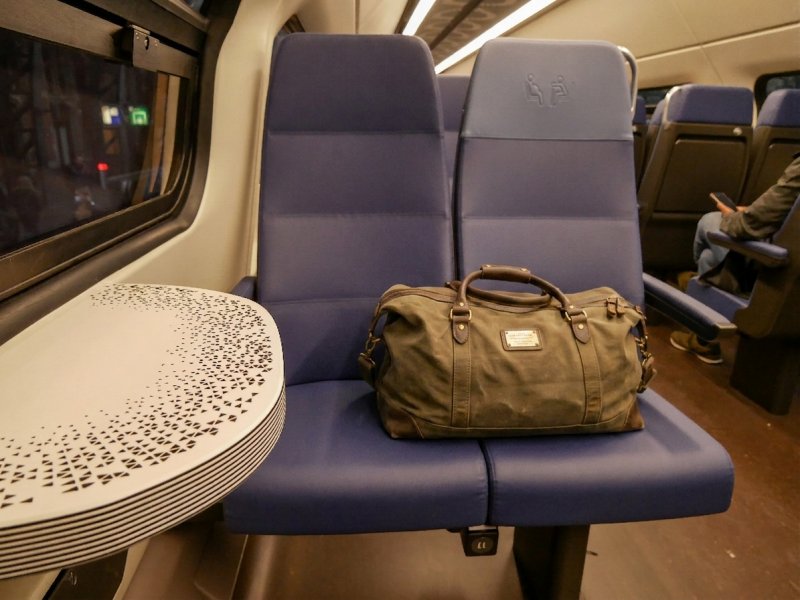 Er komt geen verbod voor tassen op lege treinstoelen, NS kiest voor huisregel. (Foto: Fantaglobe11 (Creative Commons) / AI bewerking)
